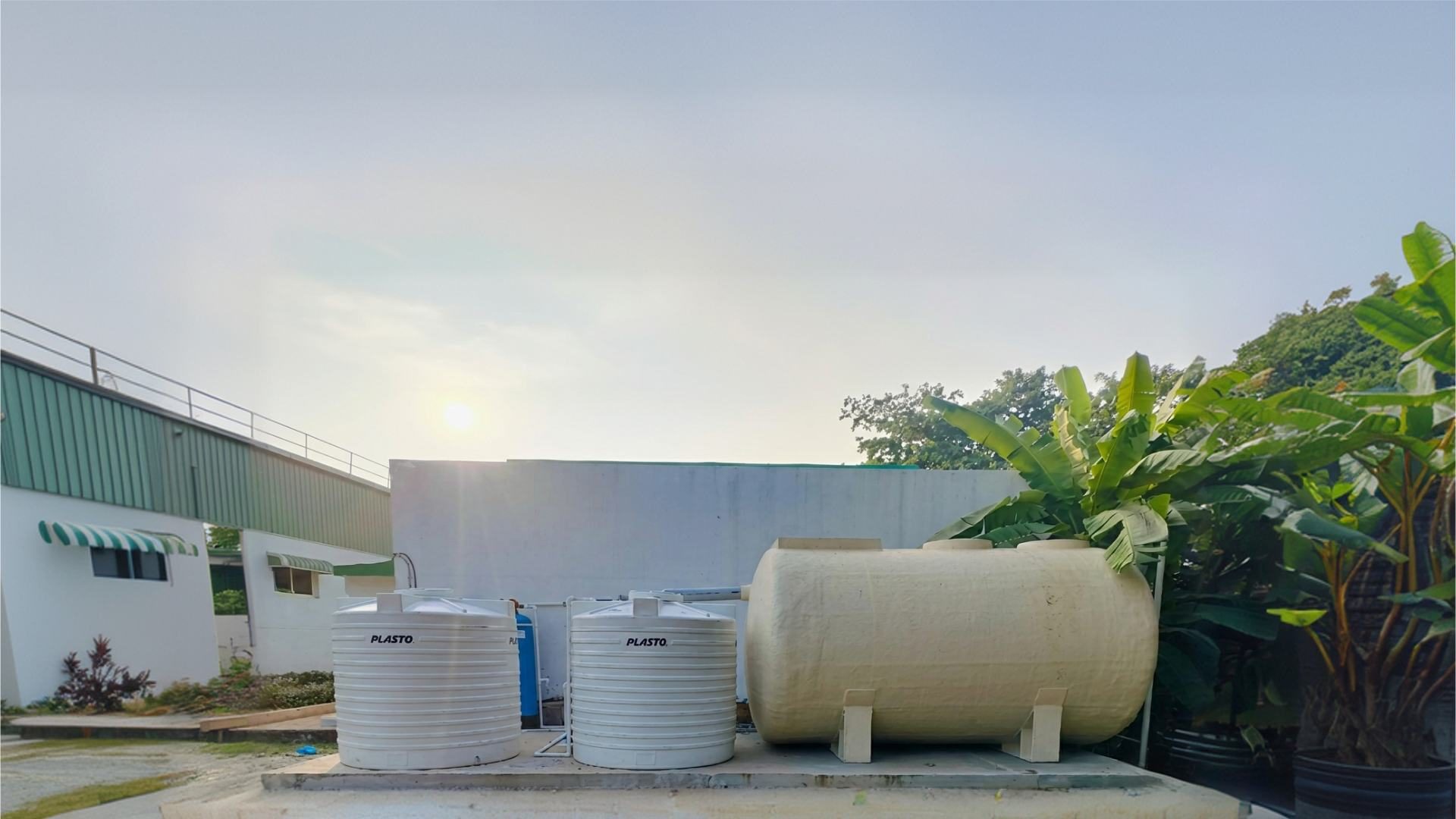 An EcoTreat plant at a partner-installed site, standing beside a building with storage tanks.